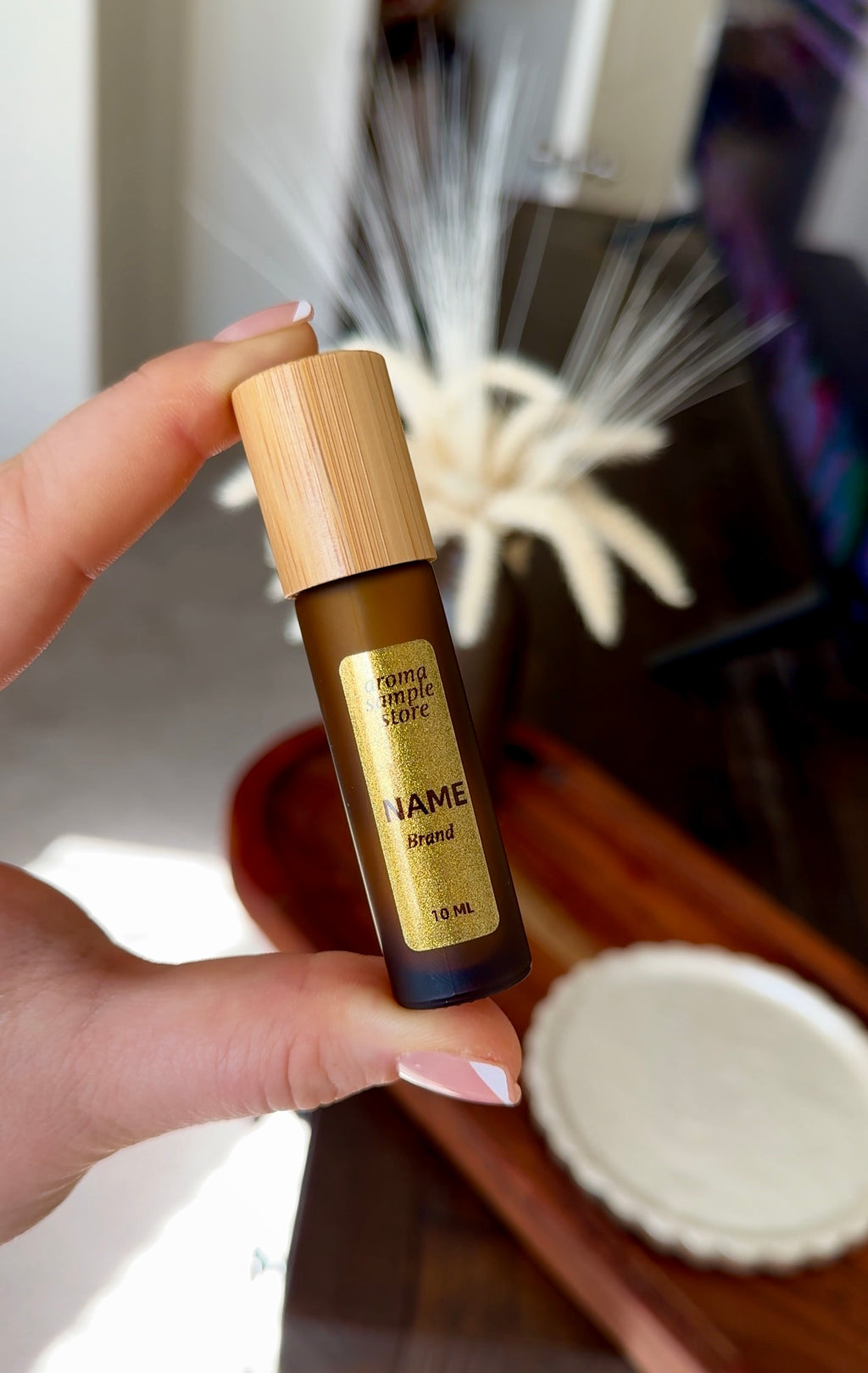 Hand holding a small rollerball bottle with a wooden cap and gold label.