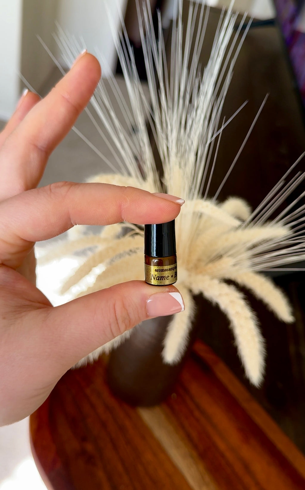 Hand holding a small bottle of perfume in front of a decorative plant